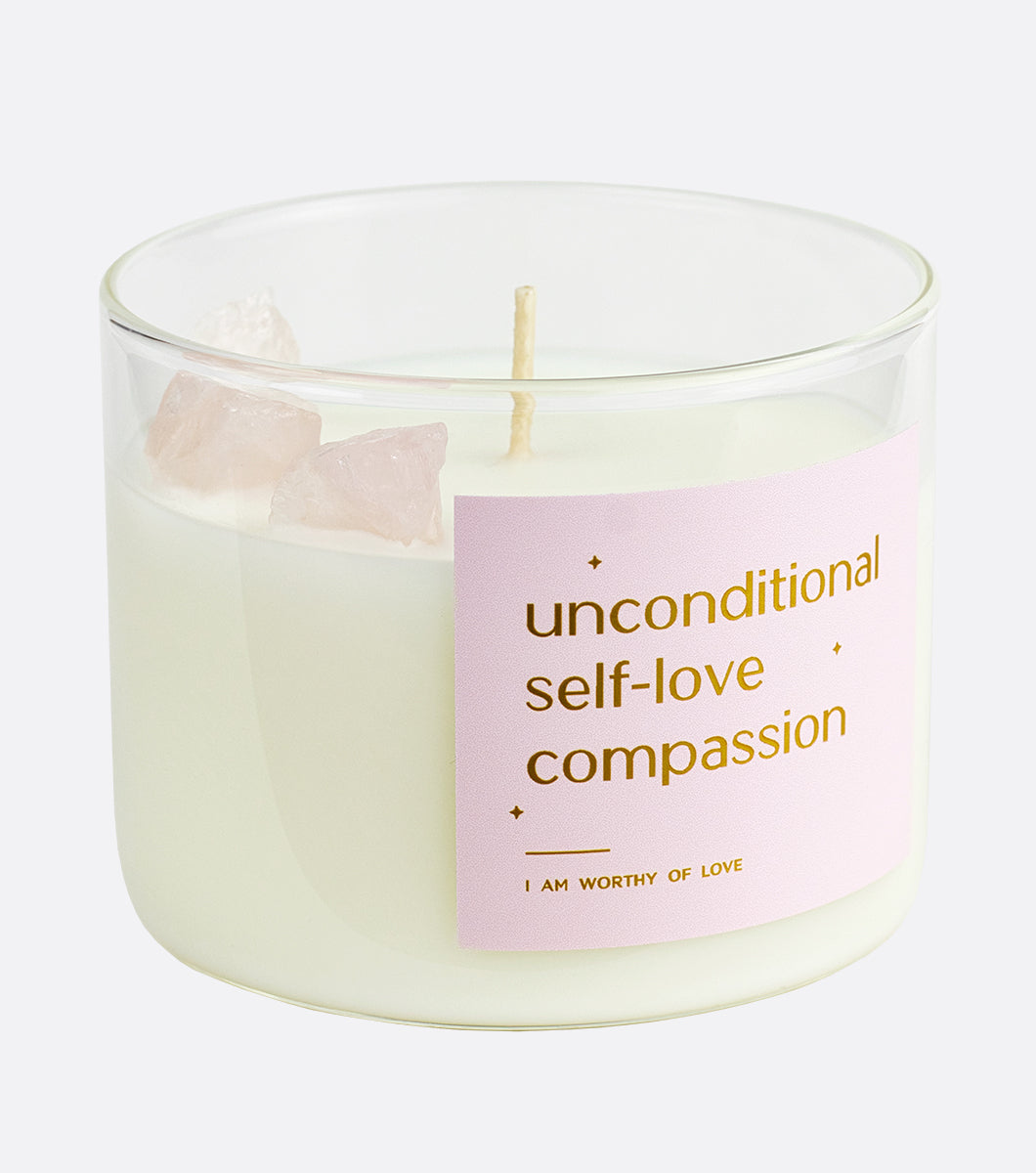 crystal candle with rose quartz crystals inside, light pink label says uncondition self-love compassion in gold foil
