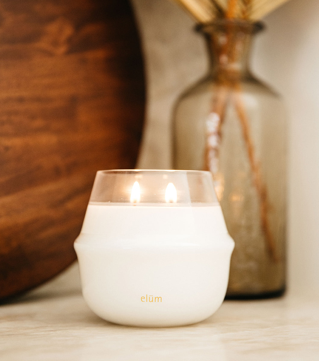 large round white classic vanilla scented candle with two wicks lit with modern home stylings in the background