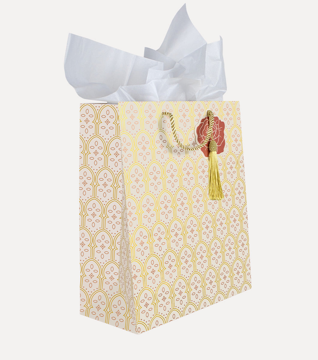 large gift bag with arched moroccan designs and rose gold foil and gold foil accents. The bag features a rose shaped hang tag, gold tassel and included white tissue paper