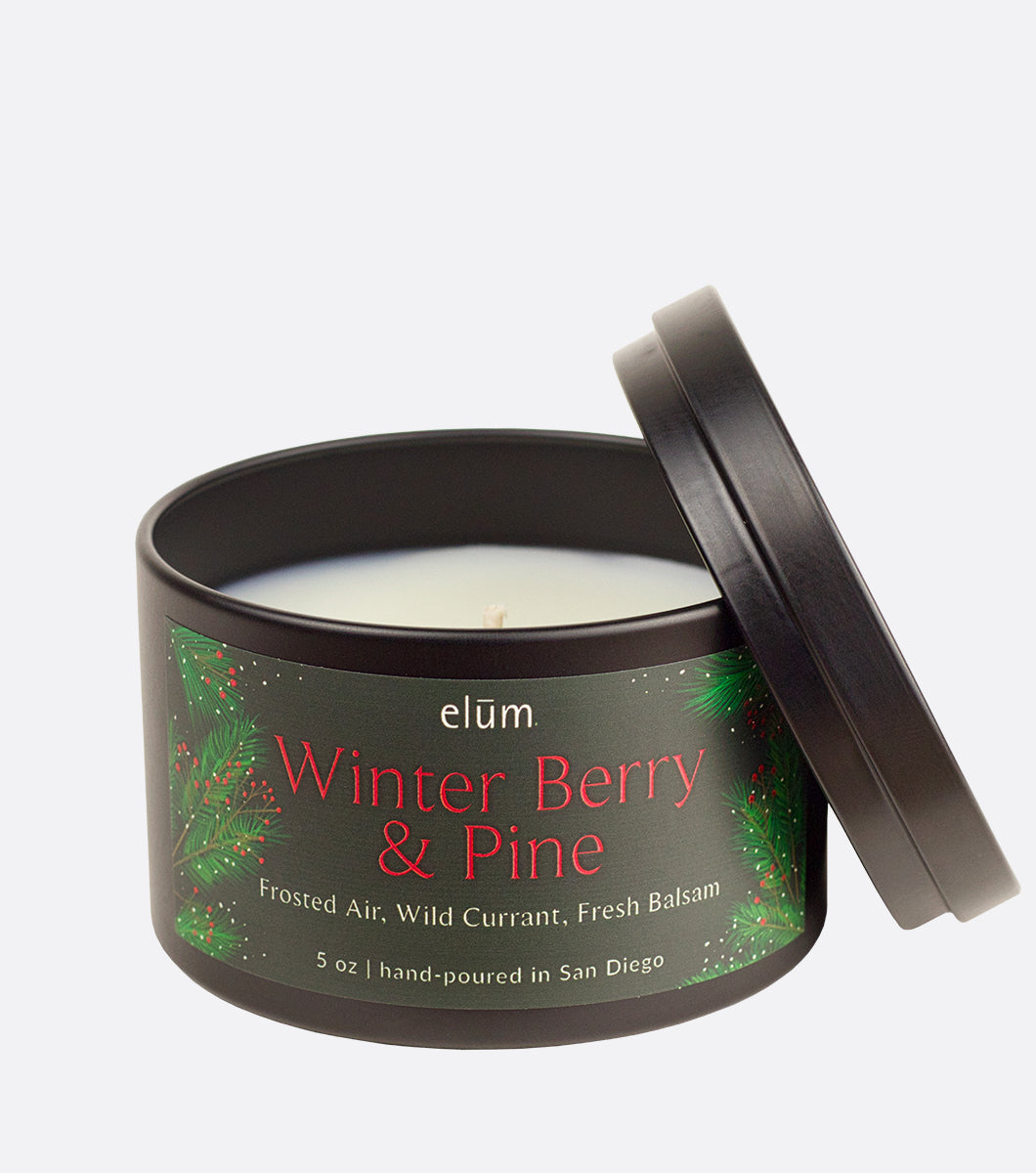 winter berry and pine holiday scented candle, black metal candle vessel with matching lid and dark green label with pine and berry design 