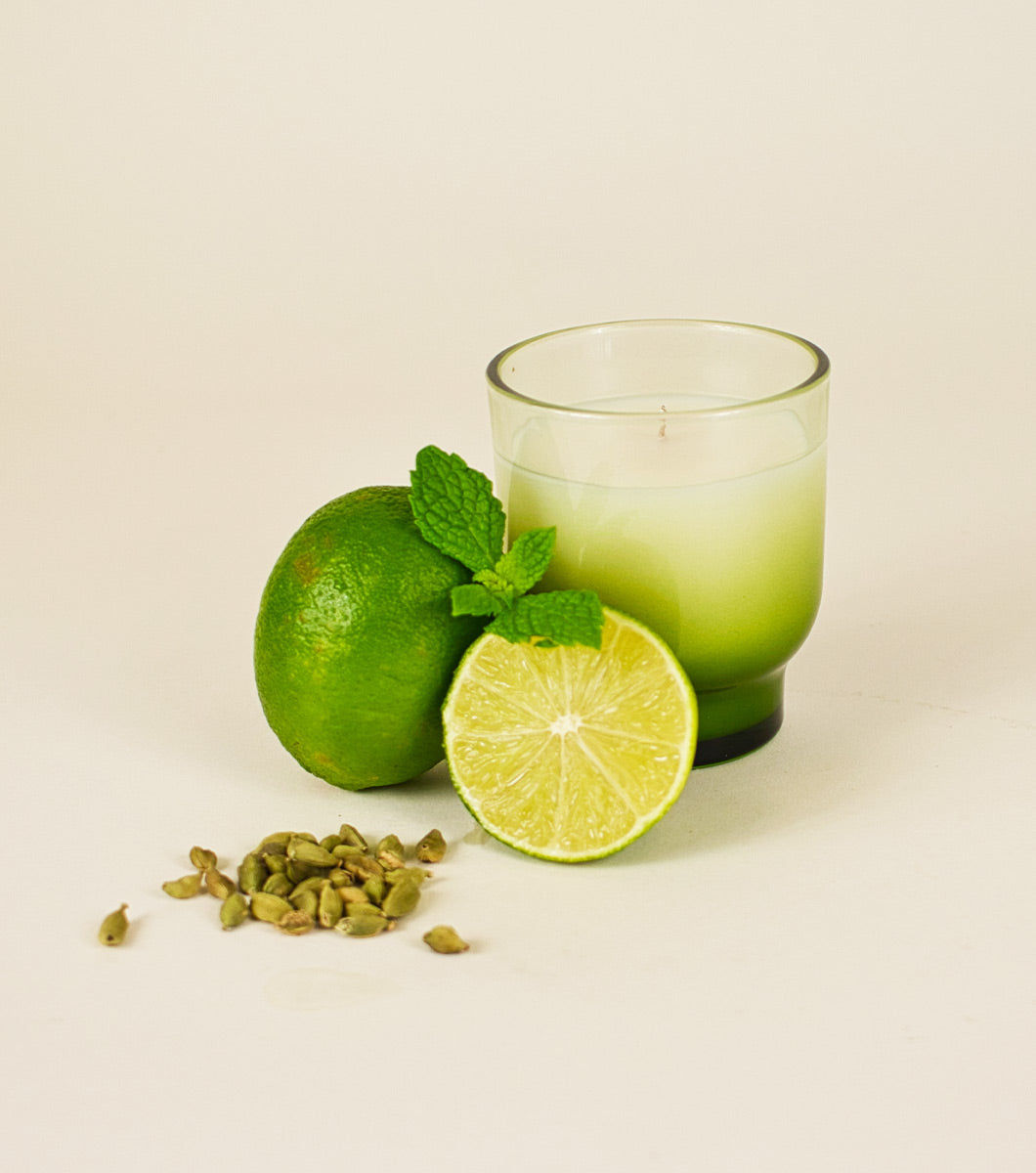 small italian bergamot scented candle posed next to sliced limes, mint and cardamom