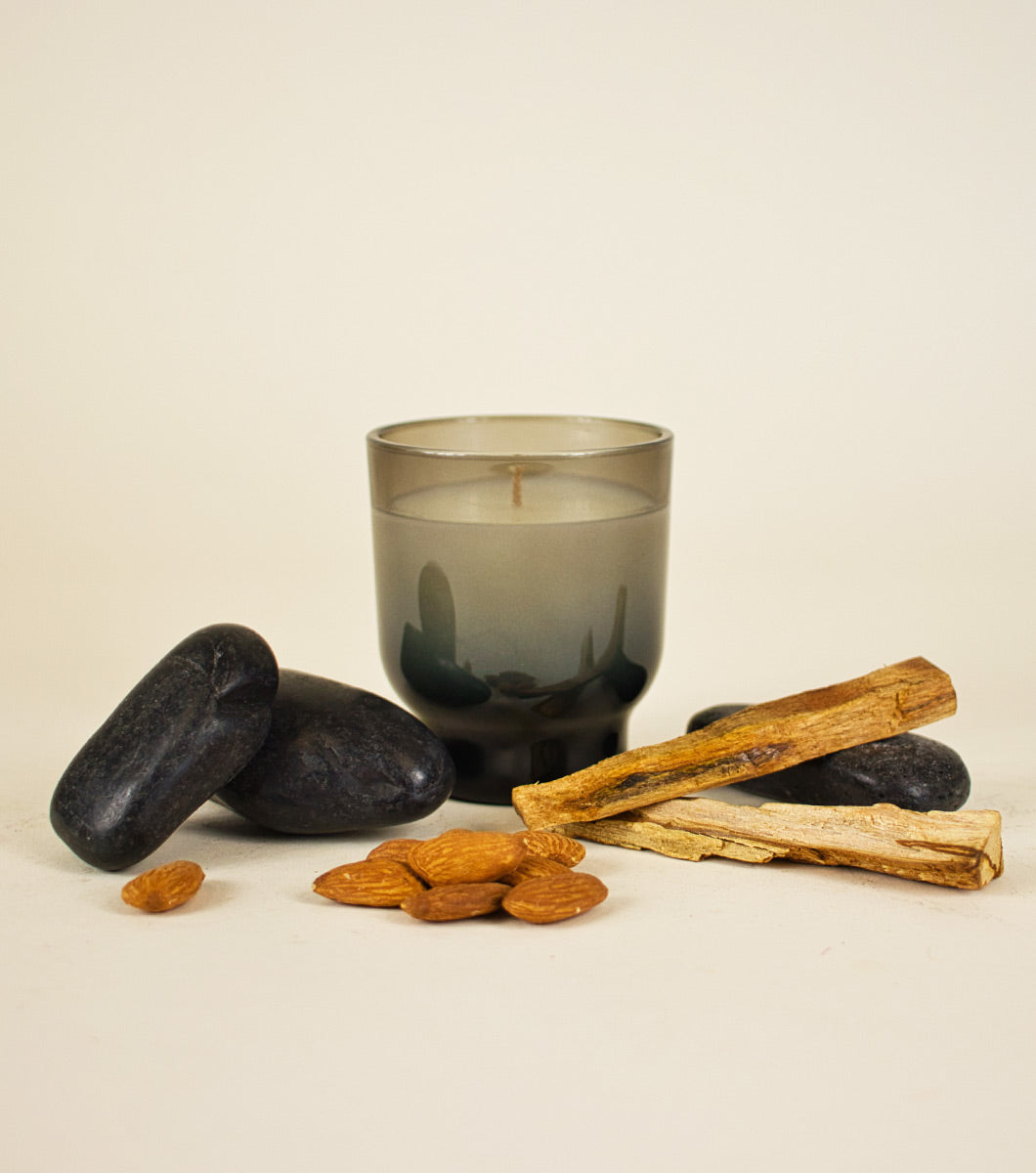 small velvet sandalwood scented candle pictured next to pieces of sandalwood, black stones and almonds