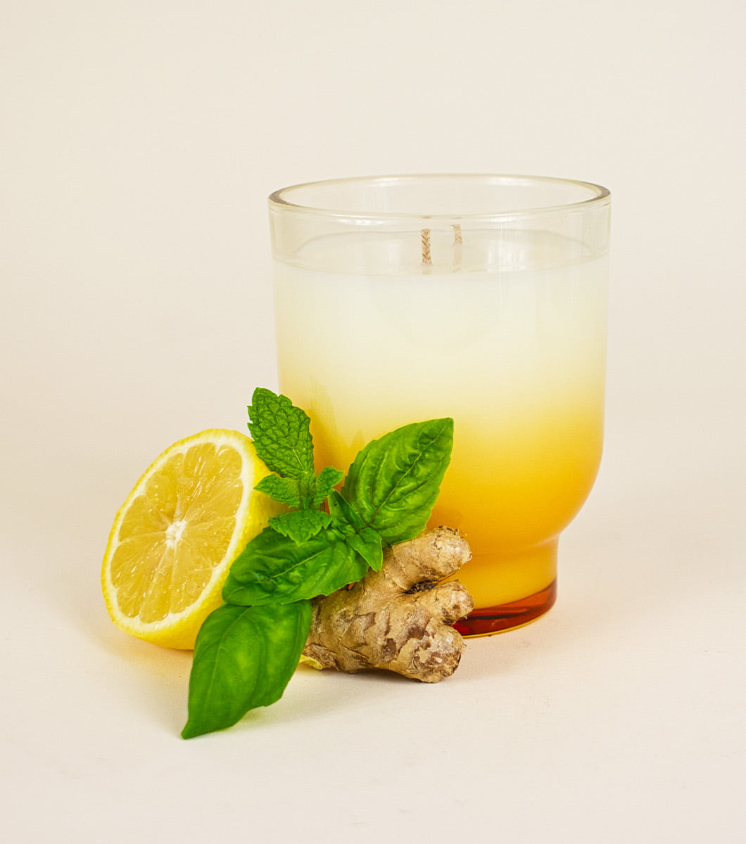 large yellow golden basil and mint scented candle pictured with lemon, ginger and sprigs of mint and basil 