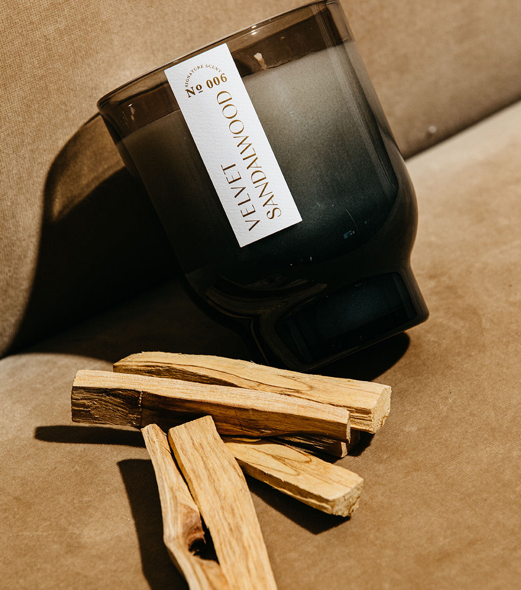 large gray and black velvet sandalwood scented candle pictured next to several sticks of sandalwood