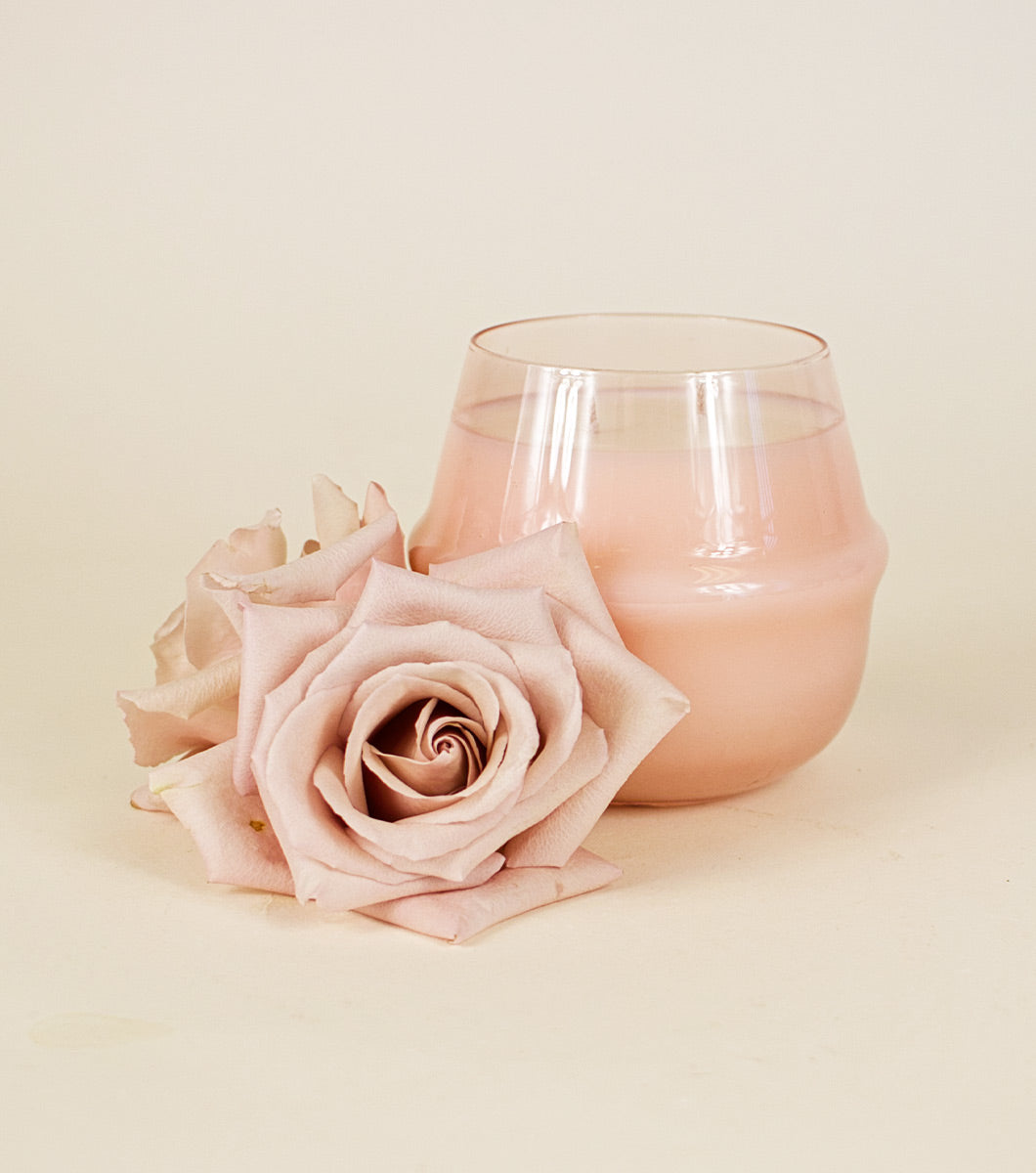 large pink moroccan rose scented candle pictured next to two light pink roses