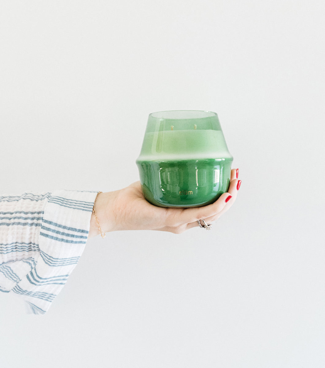 hand holding out a large green italian bergamot scented candle against a white background