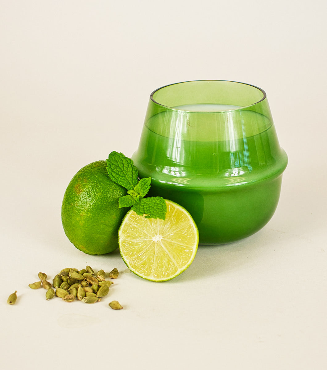 large green italian bergamot scented candle pictured with sliced limes, mint and cardamom