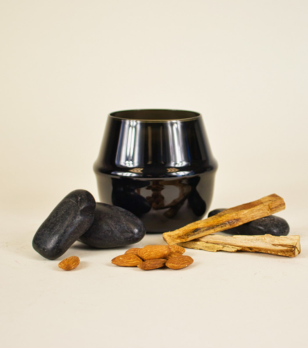 large black velvet sandalwood scented candle pictured wit hrounded black stones, sticks of sandalwood and almonds