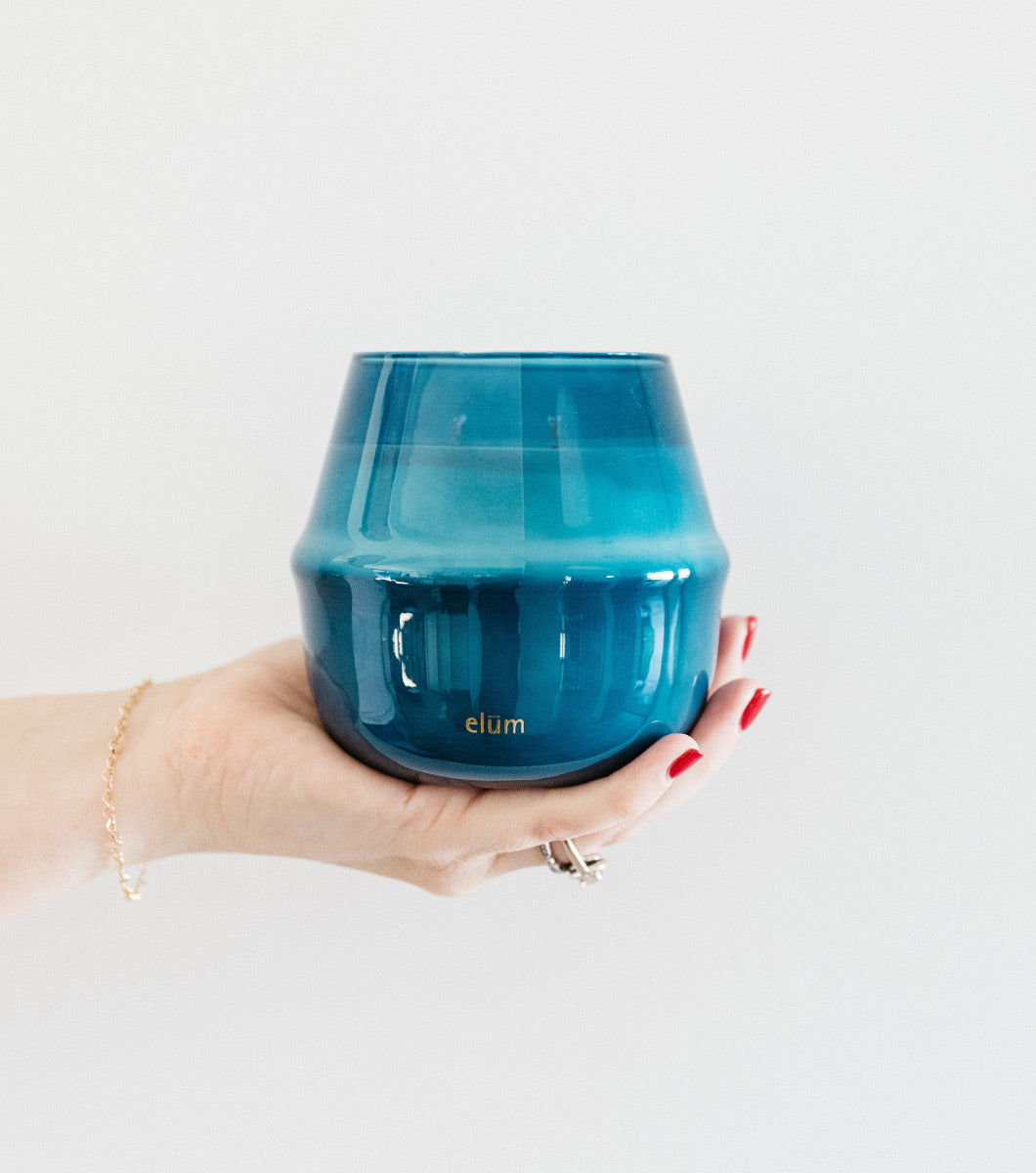 hand holding out large blue serene sea salt scented candle that has gold elum logo on the bottom of the vessel