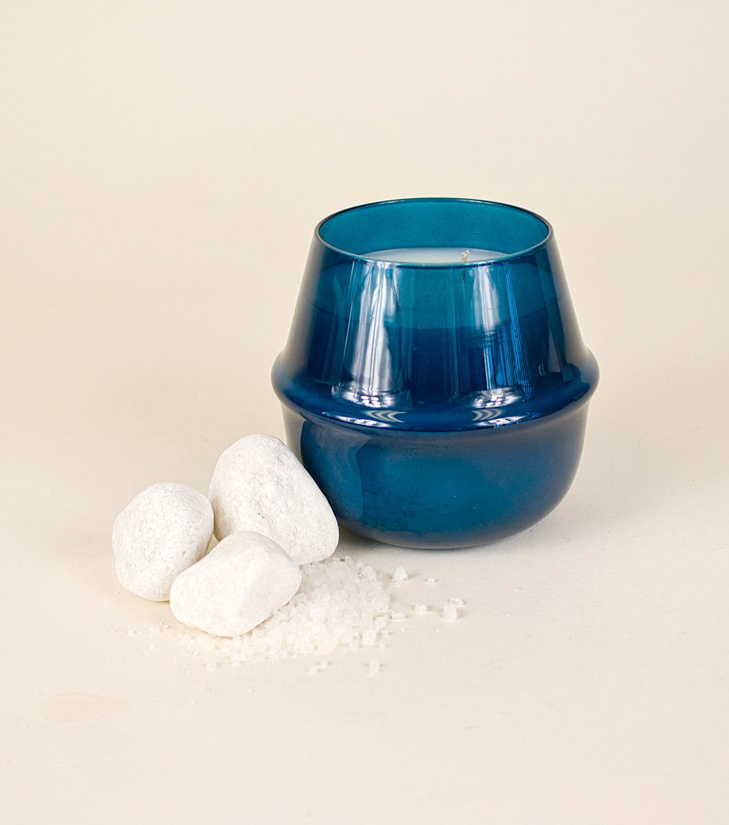 large blue serene sea salt scented candle pictured with white tones and coarse sea salt