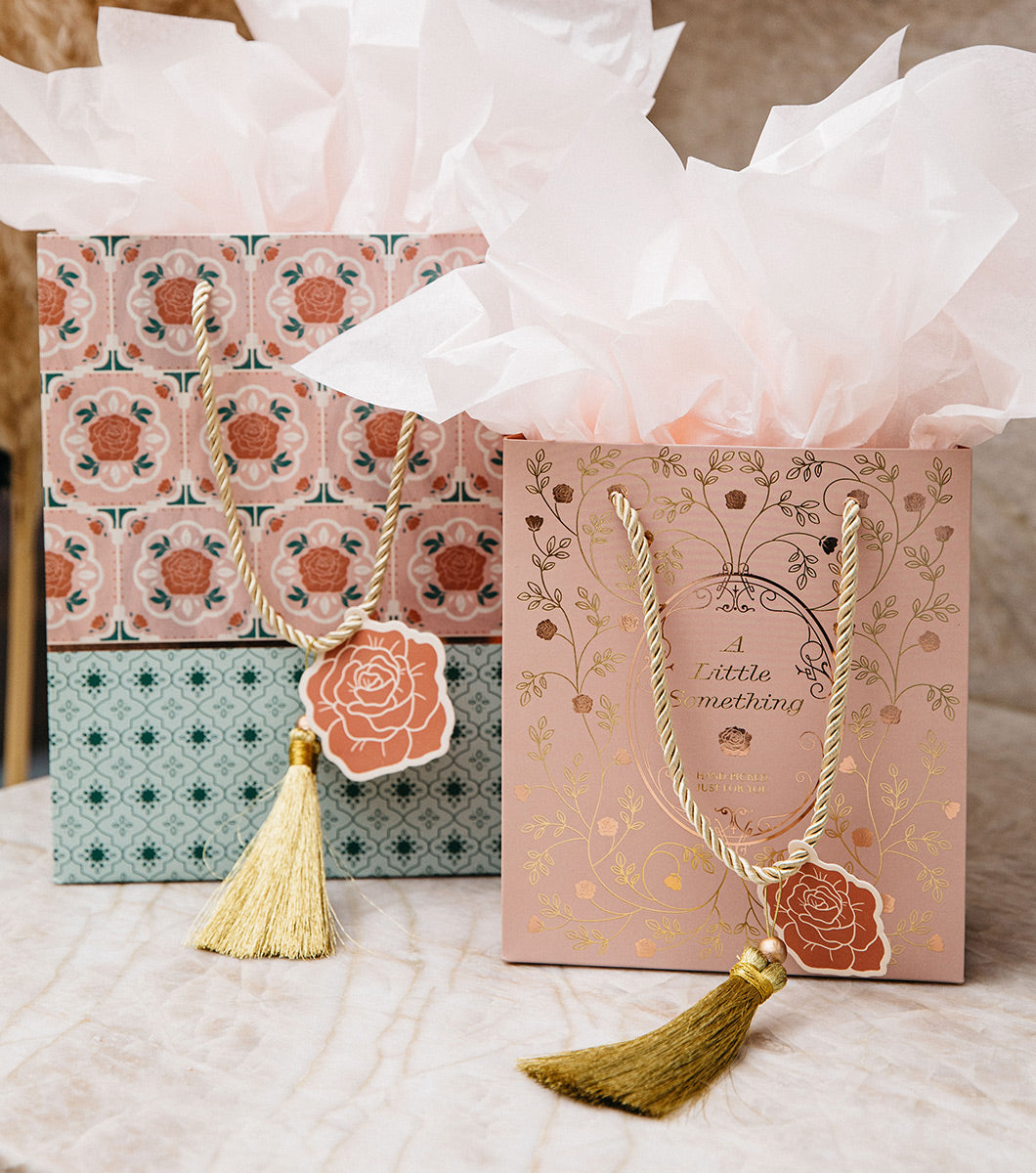 medium and small gift bags pictured together with blush pink tissue paper and gold tassels. Medium gift bag features moroccan tile design and small gift bag features vintage rose designs