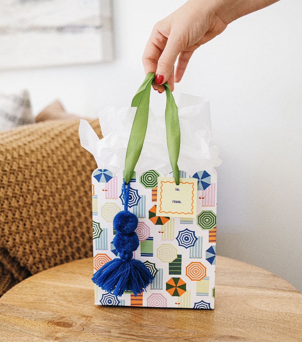 hand holding a small gift bag with designs of striped umbrellas and beach towels with white tissue paper