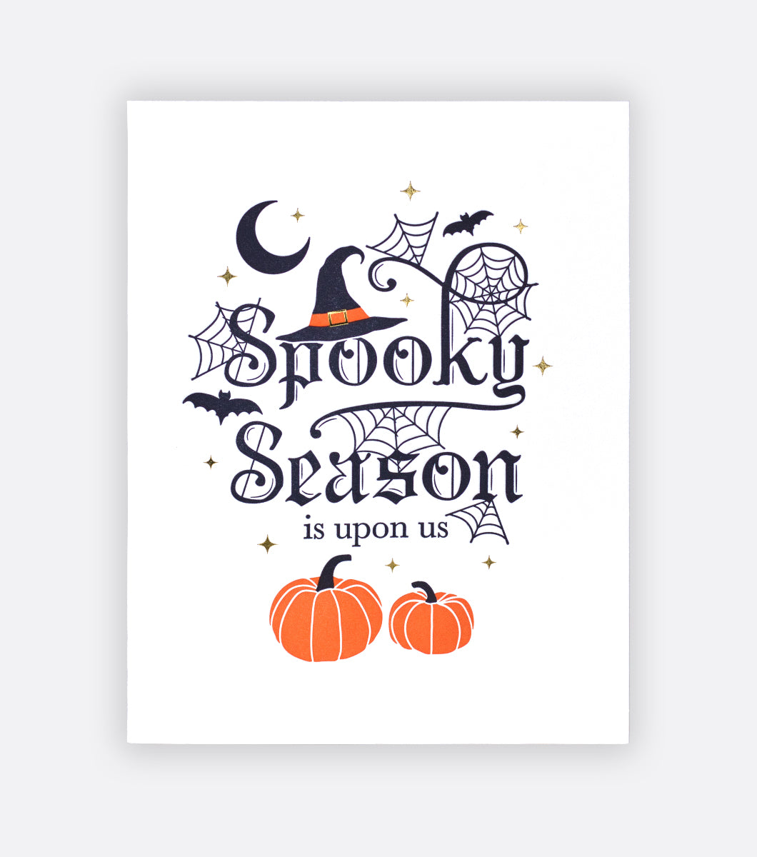 spooky season letterpress greeting card with message that says "spooky season is upon us" with a witches hat, pumpkins and spiderwebs surrounding the design